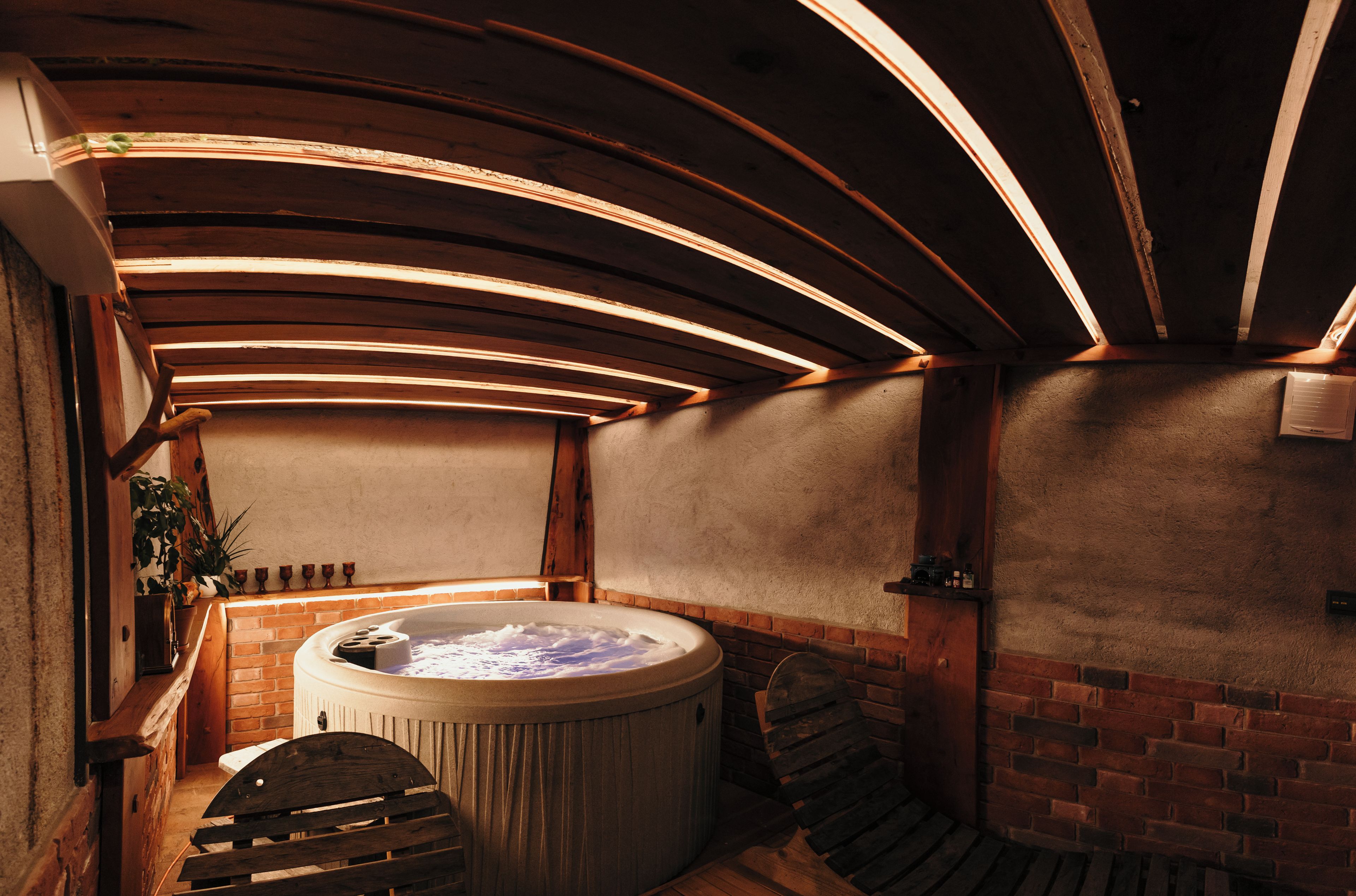 A hot tub with a brick wall and wooden beams in a cozy, dimly lit room.