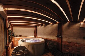 Un bain à remous avec un mur en briques et des poutres en bois, dans une pièce chaleureuse et à la lumière tamisée.