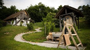 A rustic wooden cabin with a thatched roof, a wooden staircase, and a small garden area with a wooden swing set.
