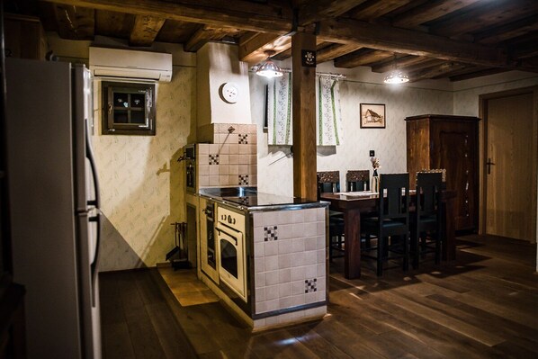 A compact kitchen with a refrigerator, stove, and dining area with chairs. - Vineyard cottage Škatlar 2 (Otočec)