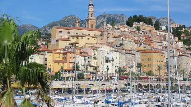 A coastal town with a prominent church tower, a marina with numerous boats, and a mountainous backdrop. - Rental small 3 Pieces Historic Center (Menton)