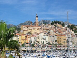 A coastal town with a prominent church tower, a marina with numerous boats, and a mountainous backdrop. - Rental small 3 Pieces Historic Center (Menton)