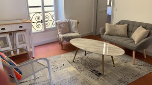 A living room with a grey sofa, a patterned armchair, a small round table, and a metal chair. - Rental small 3 Pieces Historic Center (Menton)
