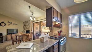 A kitchen with granite countertops, a dining area with wooden chairs, a built-in oven, and a window with blinds. - Condo on Golf Course: 2 Mi to Grindstone Lake! (Ruidoso)