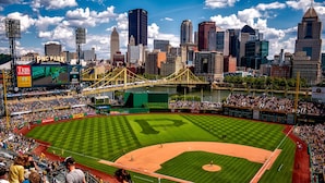 A baseball stadium with a large seating area, a field, and a city skyline in the background. - Stay Alfred Cultural District (Pittsburgh)