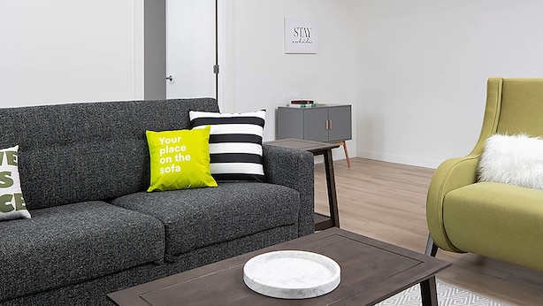 A modern living room with a grey sofa, a green armchair, a small table, and a cabinet. - Stay Alfred Cultural District (Pittsburgh)