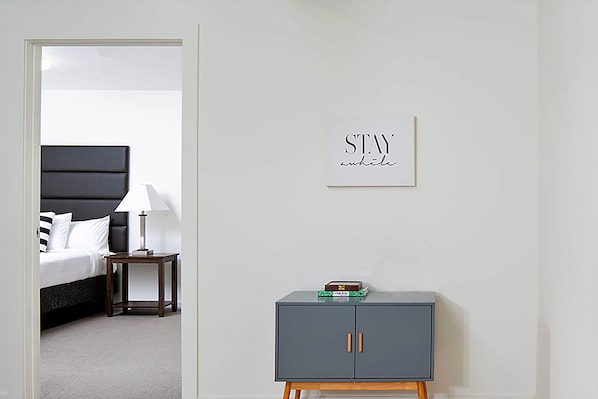 A bedroom with a bed, bedside table, lamp, and a grey cabinet with a sign on the wall.