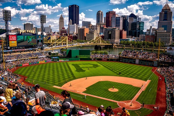 A baseball stadium with a large seating area, a field, and a city skyline in the background. - Stay Alfred on Penn Avenue (Pittsburgh)