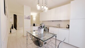 Una cocina moderna con armarios blancos, una mesa de comedor de vidrio y luces colgantes.