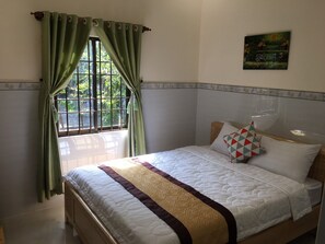 Relax in a serene bedroom with a large bed, a painting above, and a window with green curtains.