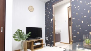 A living room with a flat-screen TV on a wooden stand, a potted plant, and a glass coffee table. - Ko's Apartment, Tatsumi West Station (Osaka)