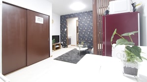 A room with a large wardrobe, a small table with a plant, a microwave, and a television. - Ko's Apartment, Tatsumi West Station (Osaka)