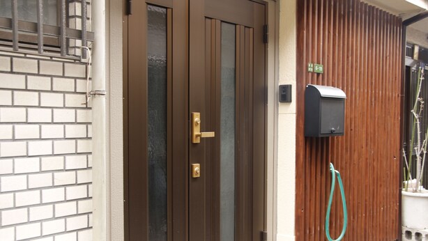 A brown door with a glass panel, a mailbox, and a green hose on a wooden fence. - Ko's Apartment, Tatsumi West Station (Osaka)