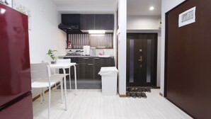 A compact kitchen with white cabinets, a red refrigerator, and a dining area with a white table and chairs. - Ko's Apartment, Tatsumi West Station (Osaka)