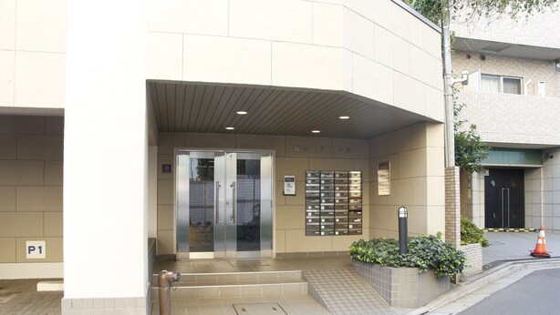 L’entrée d’un hôtel, avec une porte en verre, un petit espace extérieur aménagé en coin salon et un panneau indiquant le parking, portant la mention « P1 ».