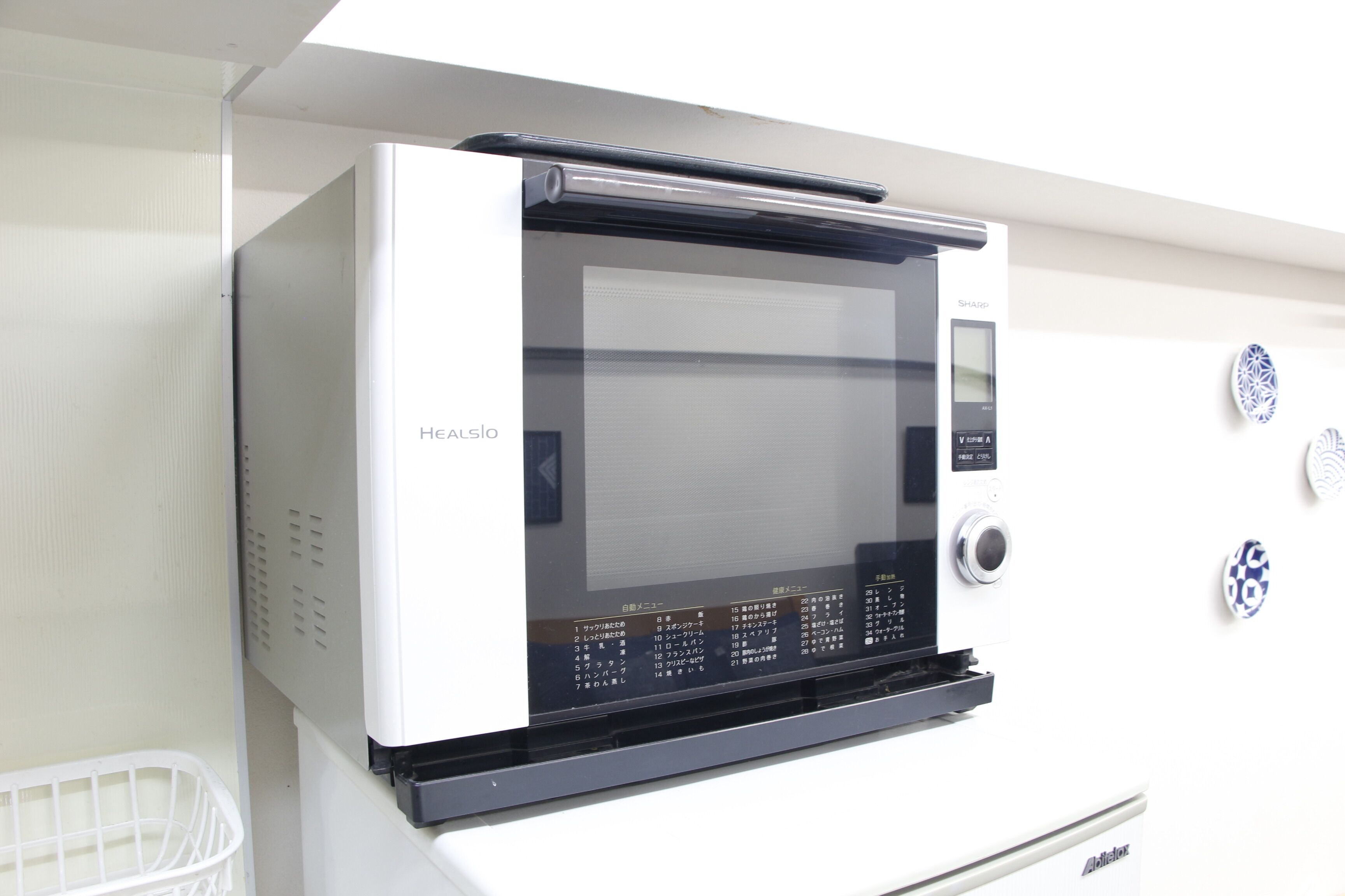 Horno microondas blanco y negro con pantalla digital y panel de control, colocado sobre un gabinete blanco.