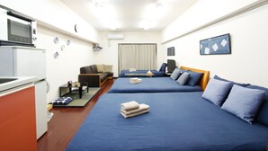 Une chambre d’hôtel compacte comprenant un coin cuisine, deux lits avec une literie bleue, un canapé et un téléviseur.