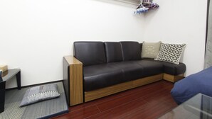 Un salon moderne avec un canapé en cuir noir, une table d’appoint en bois, un coussin à motifs et un petit tapis.