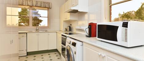 Une cuisine moderne avec des meubles blancs, un lave-linge, un four à micro-ondes et une fenêtre donnant sur les arbres.