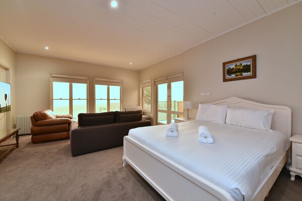 A hotel room with a large bed, a sofa, a desk, and a view of the sea through the windows.