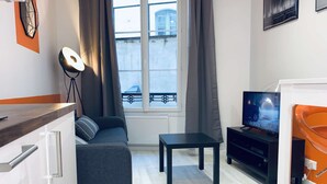 En moderne stue med en grå sofa, et lille bord, et fjernsyn og en balkon med gelænder.