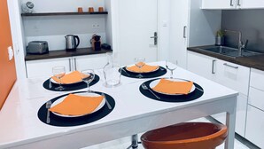 Et moderne køkken med hvide skabe, en træbordplade og et spisebord dækket med orange servietter og tallerkener.