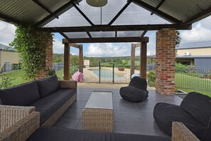 Een overdekt terras met rieten meubels, een zwembad en uitzicht op het landschap.