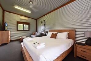 A hotel room with a large bed, a desk, a chair, a TV, and a window with a view of trees.