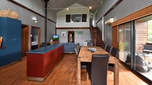 Een moderne keuken met een centraal eiland, een eethoek met een houten tafel en stoelen, en een trap die naar een bovenverdieping leidt.