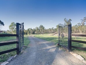 A gravel path leading through a metal gate into a grassy area with trees in the background.