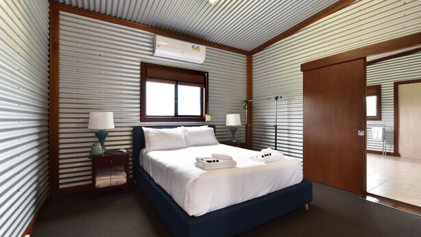 A hotel room with a bed, two bedside tables, a window, an air conditioning unit, and a door.