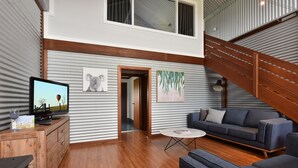A modern living room with a flat-screen TV, a wooden cabinet, a grey sofa, and a staircase.