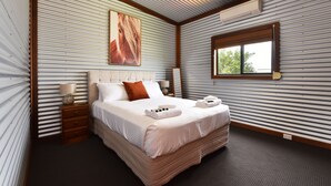 Een hotelkamer met een groot bed, een nachtkastje, een lamp, een raam en een airconditioner.