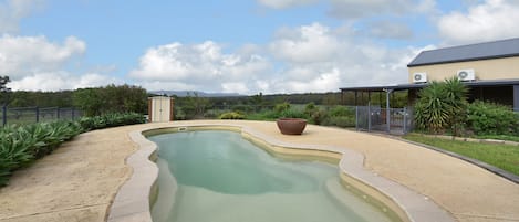 Une piscine à bordures courbes, entourée d’une terrasse en béton et d’une clôture en métal.