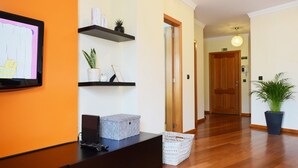 Un espace d’accueil avec un téléviseur, des étagères ornées d’objets décoratifs, un panier et une plante en pot.