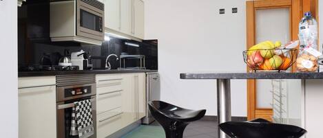 Een moderne keuken met roestvrijstalen apparatuur, een zwarte barstoel en een fruitmand op het aanrecht.