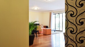 Un vaste espace de vie doté d’un plancher en bois, d’un fauteuil noir, d’un canapé rose et d’une grande fenêtre offrant une vue dégagée.