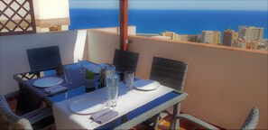 Une table à manger dressée pour deux personnes, avec vue sur l’océan et le paysage urbain.
