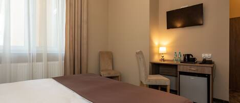 Una habitación de hotel con una cama, un escritorio con lámpara, una silla y un refrigerador pequeño.