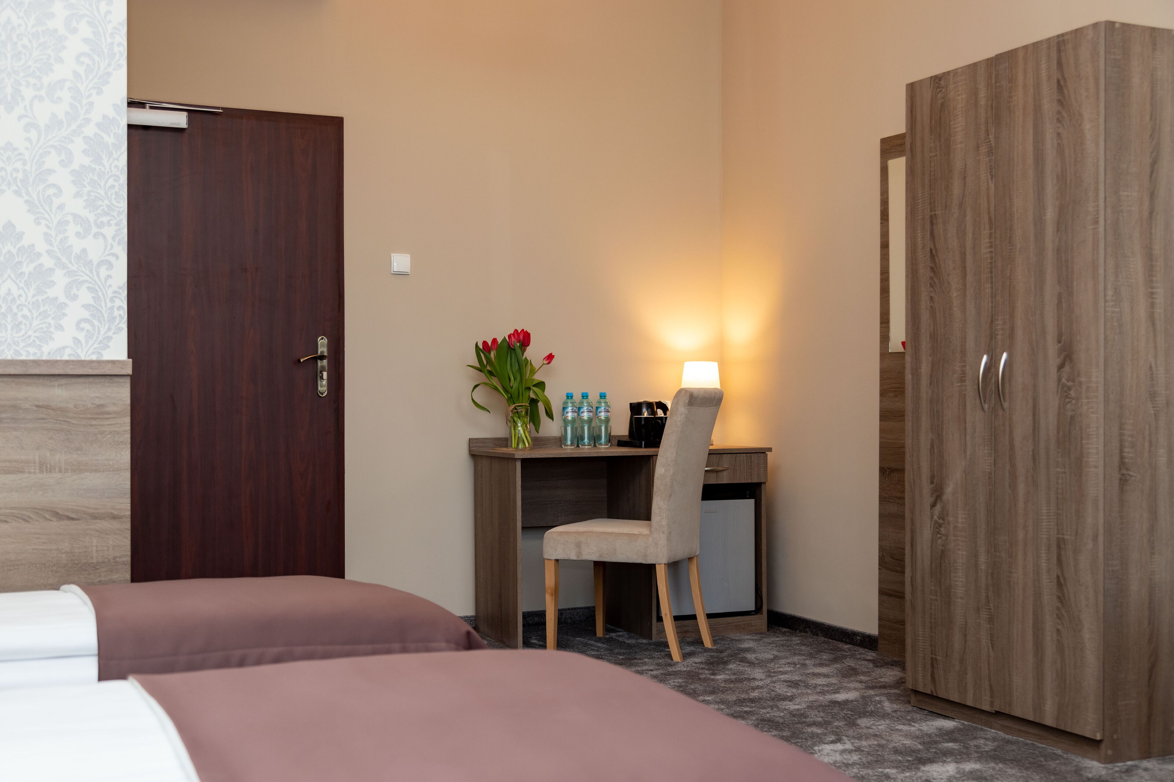 Ein Hotelzimmer mit einem Bett, einem Schreibtisch mit Stuhl, einem Kleiderschrank und einer Wandlampe.