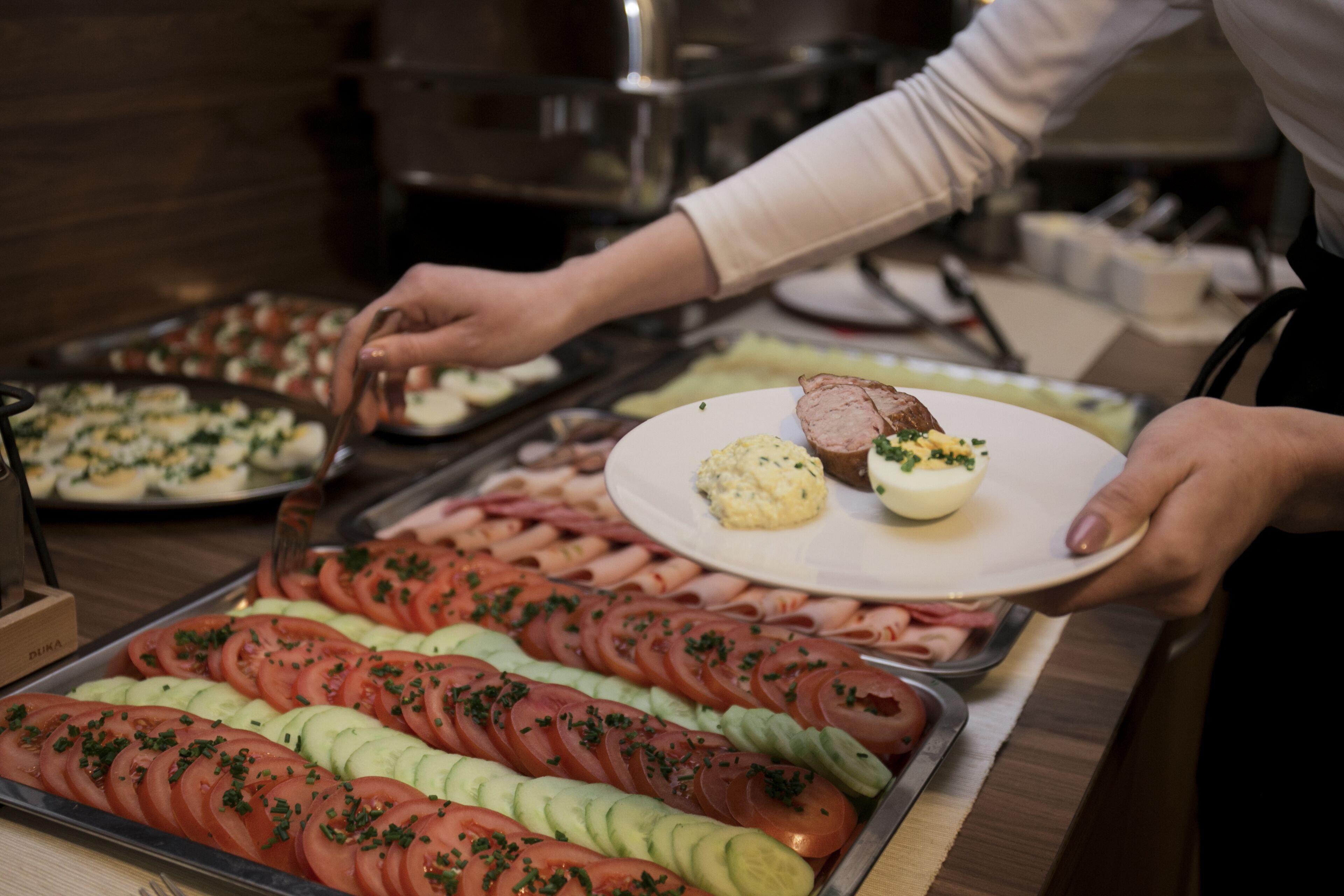 Ein Buffet mit verschiedenen Speisen, darunter Tomatenscheiben, Gurken und ein Teller mit einem Fleischgericht.