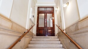 Una gran escalera con peldaños de mármol y barandillas de madera que conduce a una amplia puerta de madera con paneles de vidrio.