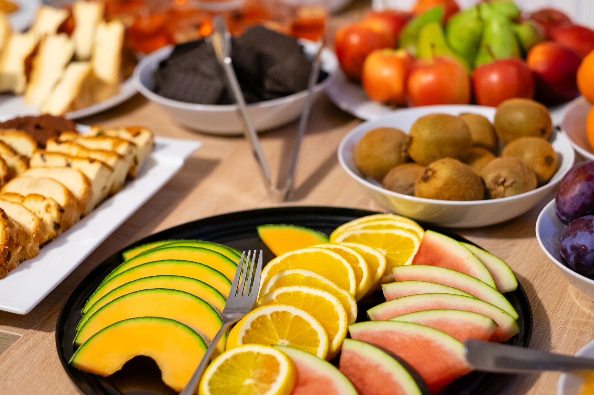Una mesa con diversos alimentos, entre ellos frutas y verduras en rodajas, dispuestas en platos.