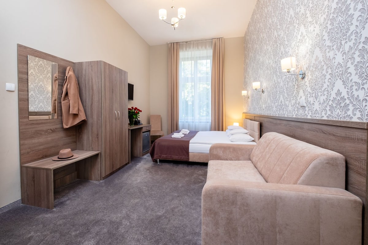 Una habitación de hotel con cama, sofá, escritorio, espejo y armario.
