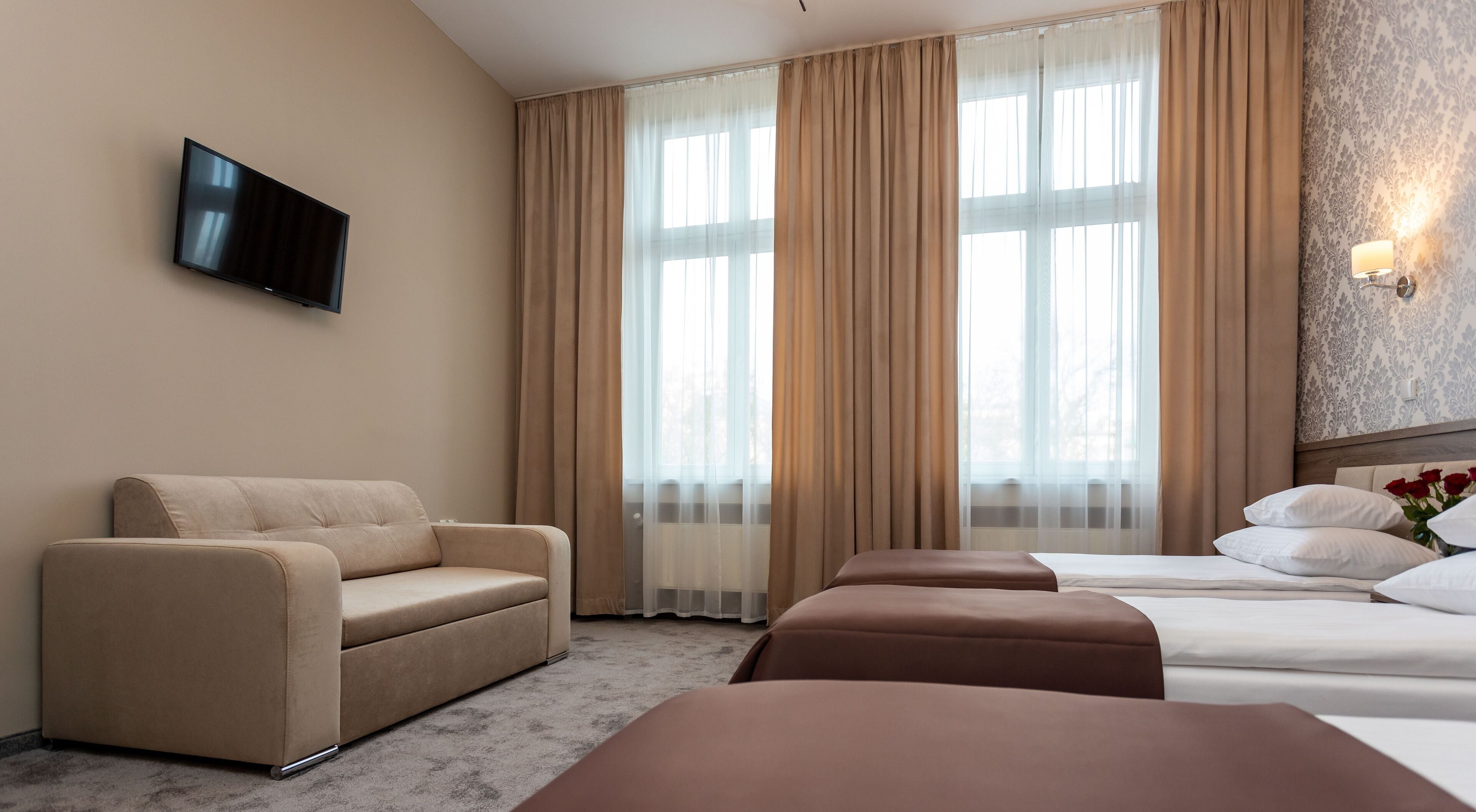 A hotel room with a sofa, a bed, a TV, and large windows with curtains.