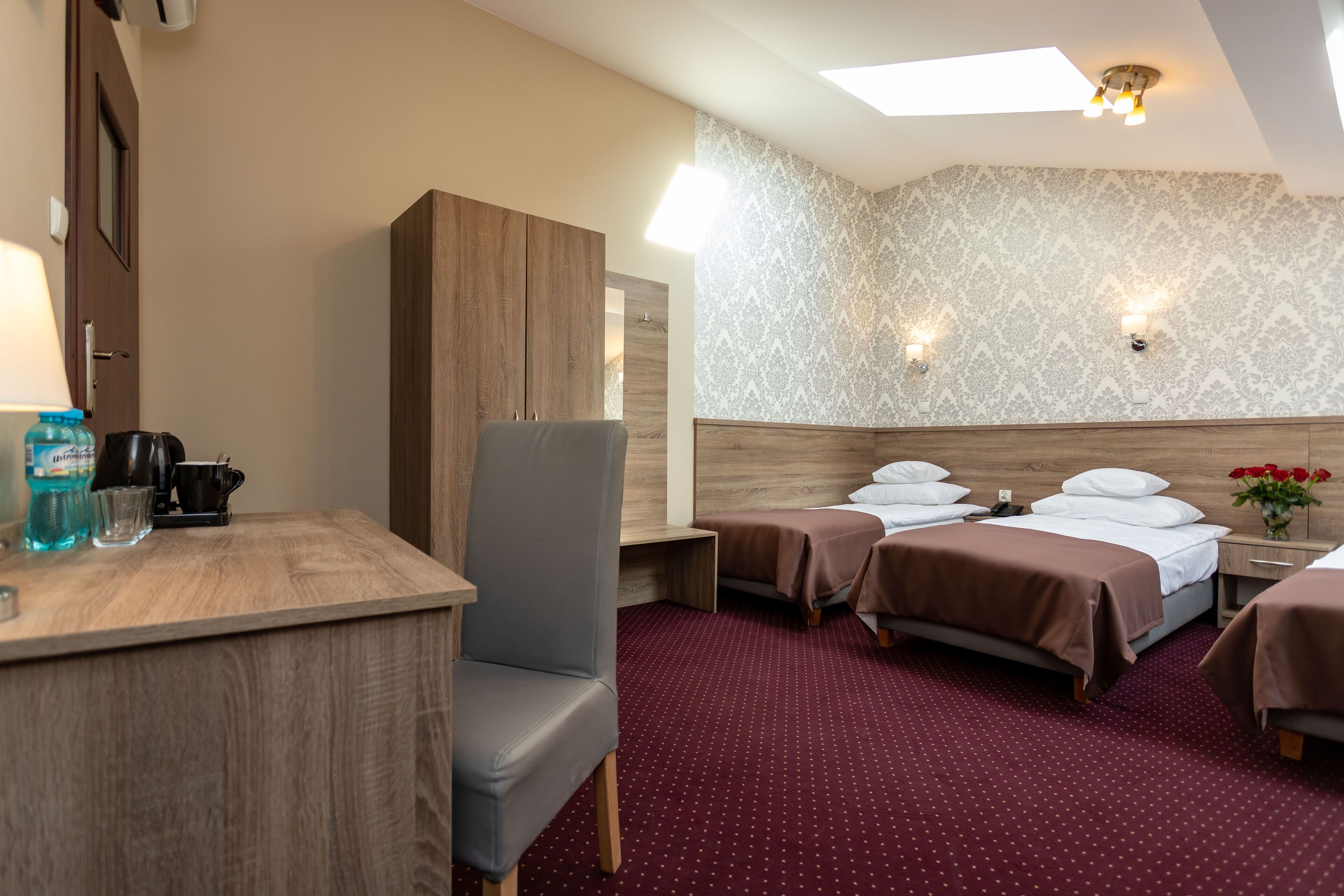 Een hotelkamer met een bureau, twee bedden, een kledingkast en een behang met patroon.