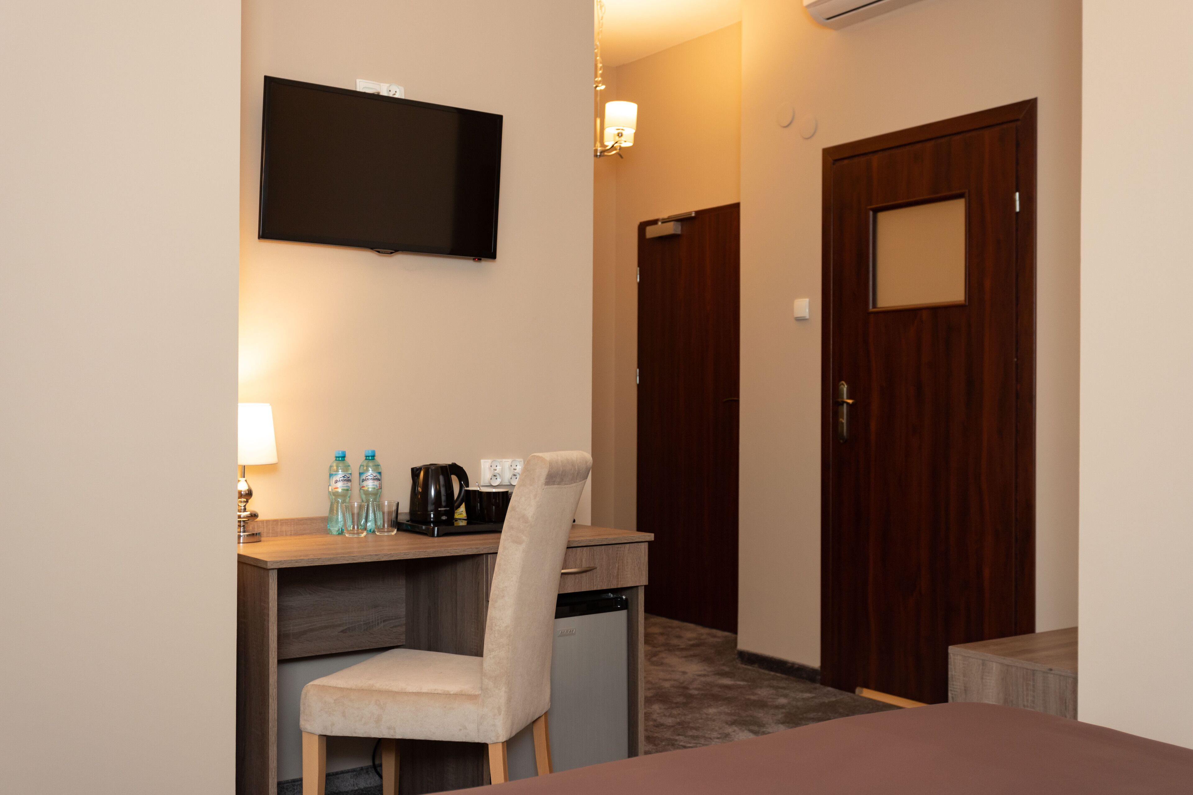 A hotel room with a desk, chair, television, and a door.