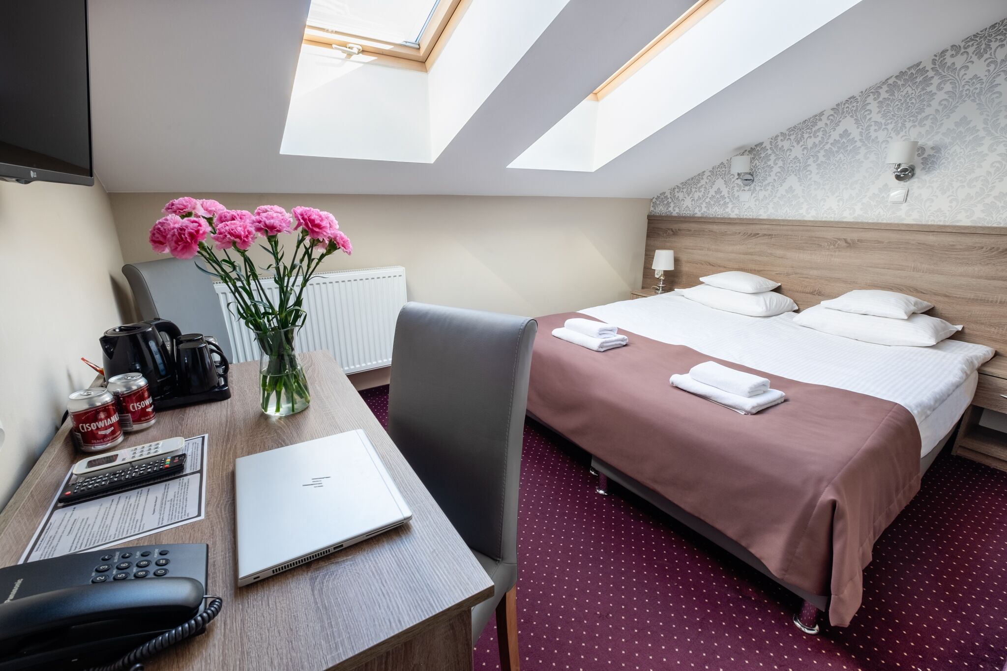 Une chambre d’hôtel avec un lit, un bureau, une chaise et une lucarne.