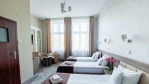 Una habitación de hotel con tres camas, un escritorio, una silla y un ventanal grande con cortinas.