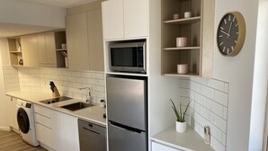 A modern kitchen with white cabinetry, stainless steel appliances, a microwave, and a clock on the wall. - Mooloolaba Beachfront Apartment (Mooloolaba)